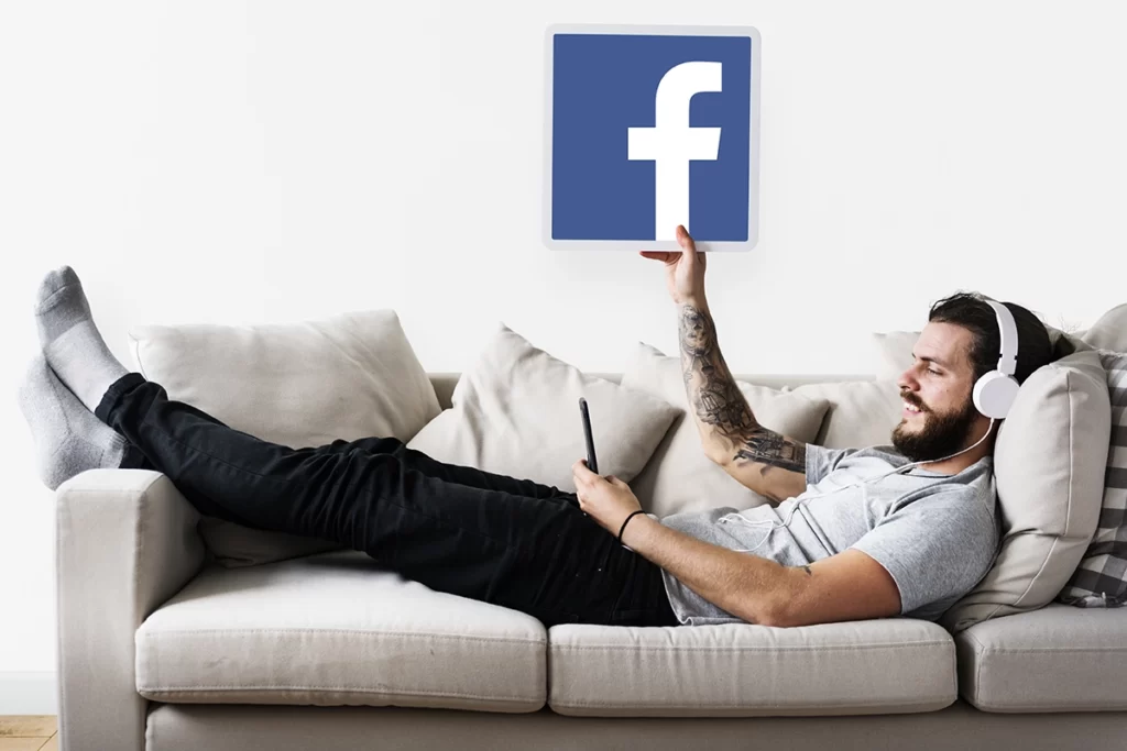 Homme allongé dans un divan montre le logo Facebook